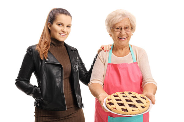 Elderly woman with an apron holding a pie and a young woman standing next to her isolated on white background