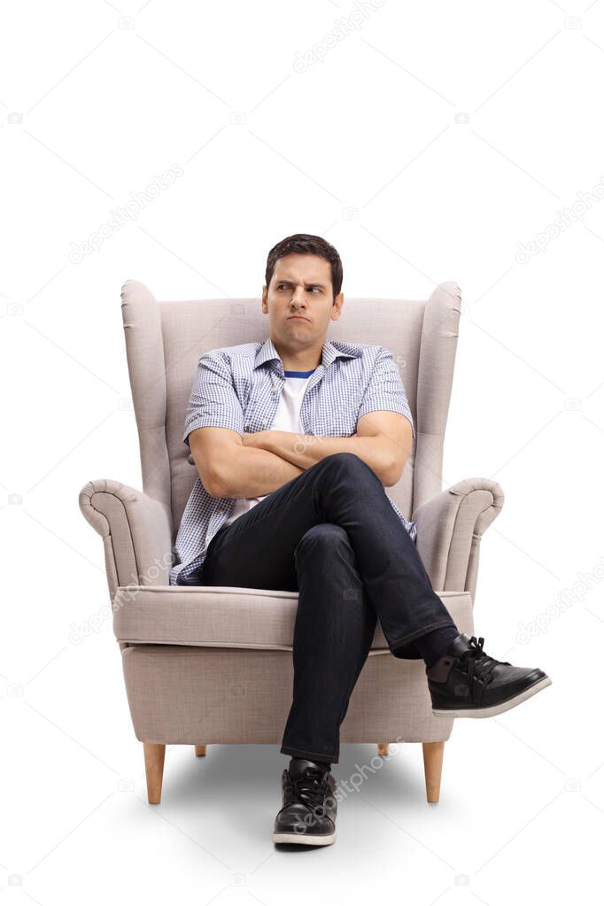 Angry young man making a grimace and sitting in armchair isolated on white background