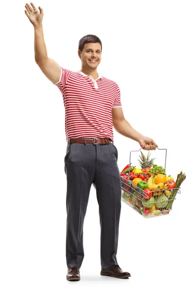 白を基調とした果物や野菜を使った買い物かごを手に手を振っている若者の全長の肖像画 — ストック写真