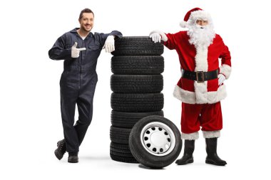 Otomobil tamircisi bir yığın lastiği işaret ediyor ve Noel Baba ile poz veriyor beyaz arka planda izole edilmiş.