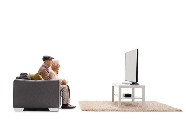 一张老年男女坐在沙发上观看白色背景的电视的侧面照片 — 图库照片