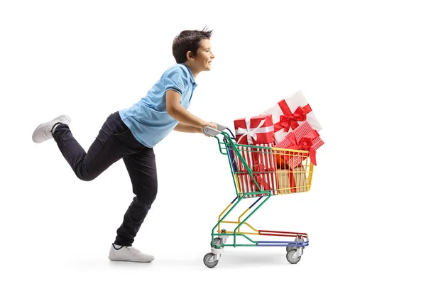 男の子が走っていて 白い背景に孤立したプレゼントとショッピングカートを押すの全長プロファイルショット — ストック写真