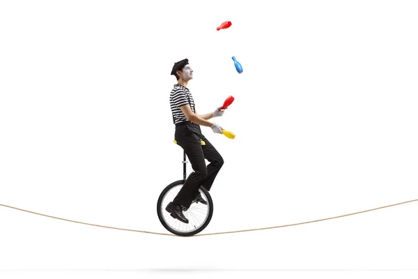 ロープの上でモノサイクルに乗って白い背景に隔離されたジャグリングの完全な長さのプロフィールショット — ストック写真