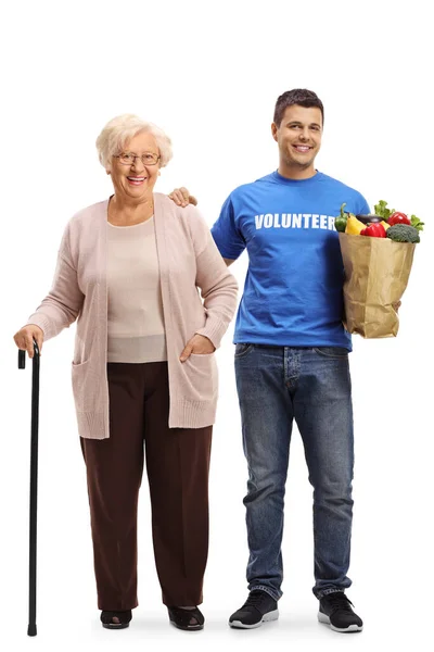 stock image Full length portrait of a senior woman standing with a young male volunteer carrying her shopping bag isolated on white background