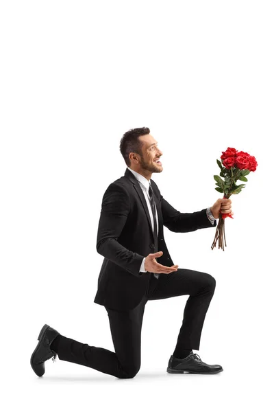 年轻英俊的男子跪在地上 手里拿着一束被白色背景隔开的红玫瑰 — 图库照片