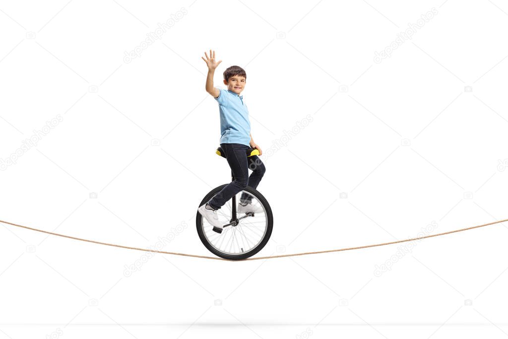Full length shot of a boy riding a unicycle on a rope and waving isolated on white background