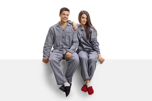 Jong Paar Dragen Dezelfde Pyjama Zitten Een Blanco Paneel Geïsoleerd — Stockfoto