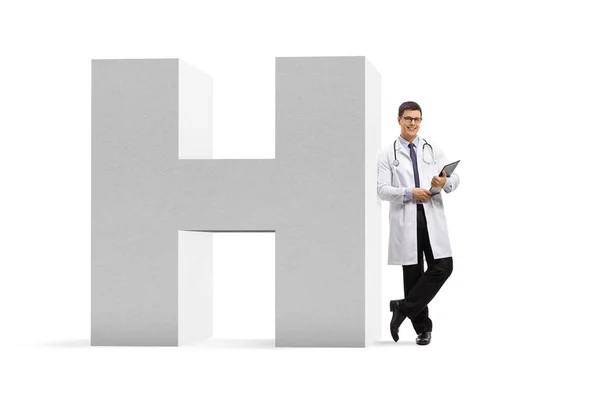 一名年轻男医生靠在一个白色背景的医院标志上的全长肖像 — 图库照片