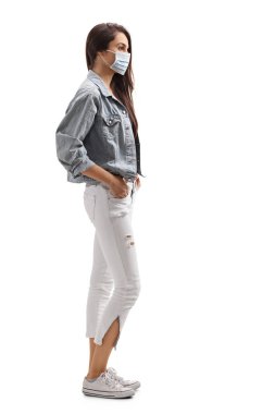 Beyaz arka planda tek başına duran koruyucu maskeli genç bir kadının tam boy profil çekimi.