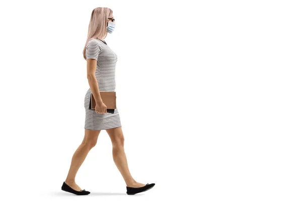若い女性のフル長プロファイルショット歩くと白い背景に隔離された保護顔マスクを身に着けています — ストック写真