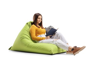 Young woman sitting on a greem beanbag chair and reading a book isolated on white background clipart