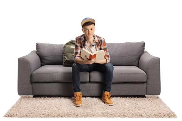 男生坐在沙发上 手里拿着一本书 看着被白色背景隔离的相机 — 图库照片