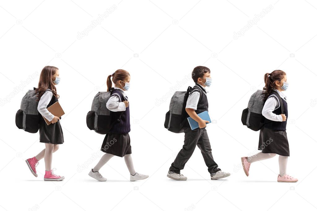 Full length profile shot of schoolchildren in uniforms walking in line and wearing protective face masks isolated on white background