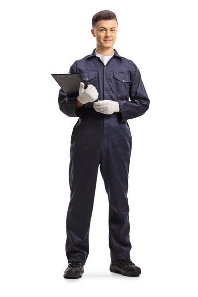 Full length portrait of a young male worker in an overall uniform holding a clipboard with a document isolated on white background