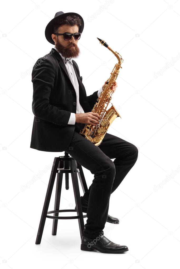 Bearded musician holding a saxophone and sitting on a chair isolated on white background
