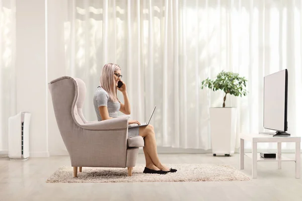 Evde Dizüstü Bilgisayarla Çalışan Koltukta Oturan Bir Cep Telefonuyla Konuşan — Stok fotoğraf