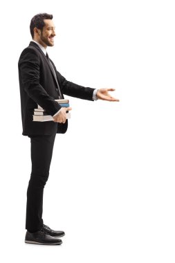 Siyah takım elbiseli bir adamın uzun metrajlı fotoğrafı. Elinde kitaplar ve beyaz arka planda el işaretleri olan bir adam.