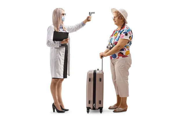 白地に隔離されたスーツケースを持つ高齢女性に温度を測定する温度計を持つ女性医師の完全な長さプロファイルショット — ストック写真