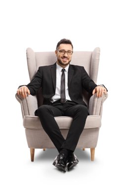 Takım elbiseli, kravatlı, gözlüklü, beyaz arka planda izole bir koltukta oturan profesyonel bir adam.
