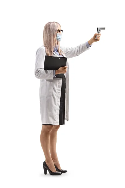 白い背景に隔離された距離赤外線温度計を保持している女性医師の完全な長さプロファイルショット — ストック写真