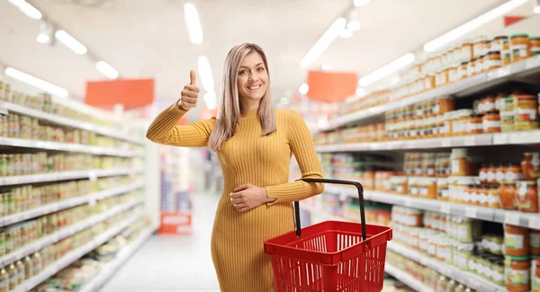 Jonge Vrouw Met Een Winkelmandje Gebaren Duimen Omhoog Een Supermarkt — Stockfoto
