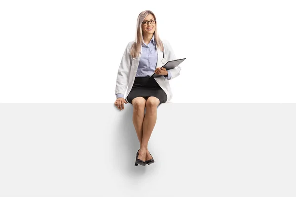 若い女性医師の完全な長さの肖像画笑顔と白の背景に隔離された空白のパネルに座って — ストック写真