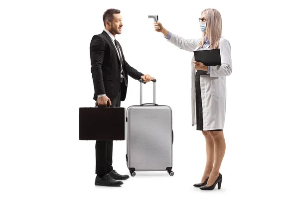 白い背景に隔離されたスーツケースを持つビジネスマンに体温計で体温を測定する女性医師の完全な長さプロファイルショット — ストック写真