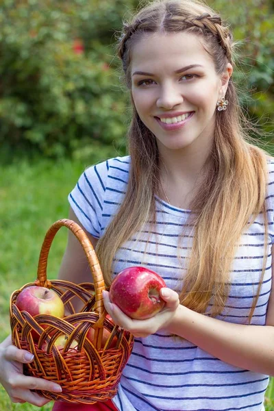 Jovem mulher bonita está deitada na grama verde. Uma menina e um cesto de maçãs vermelhas. Primavera quente . — Fotografia de Stock