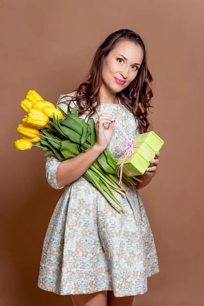 年轻漂亮的女人抱着一束黄色的郁金香和礼品盒。春天. — 图库照片