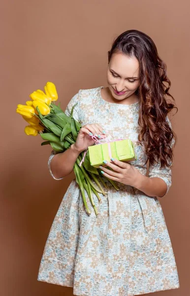 Молода красива жінка тримає букет жовтих тюльпанів і подарункову коробку. Весна . — стокове фото