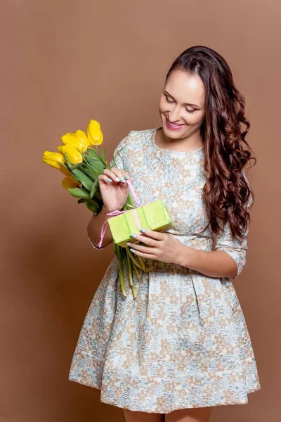 Молода красива жінка тримає букет жовтих тюльпанів і подарункову коробку. Весна . — стокове фото