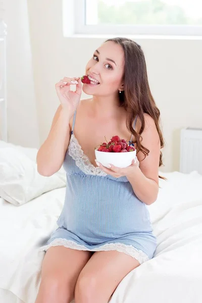 Szczęśliwy w ciąży kobieta siedzi na łóżku. Młoda kobieta w ciąży jest siedzi w sypialni. Kobieta w ciąży, relaksujące. Młody pregna — Zdjęcie stockowe