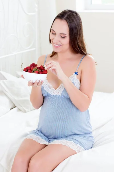 Feliz mujer embarazada sentada en la cama. Una joven embarazada está sentada en el dormitorio. Mujer embarazada relajándose. Joven pregna —  Fotos de Stock