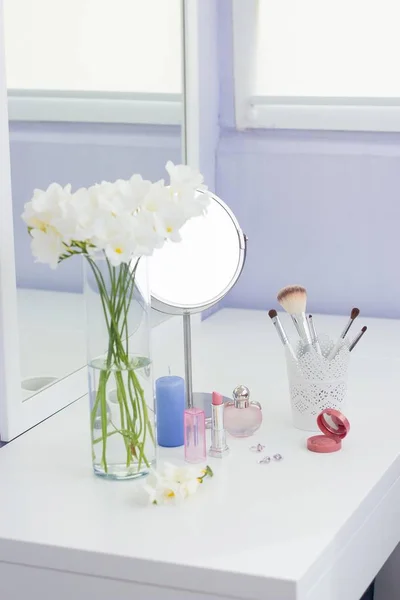 Cosmetics and a bouquet of flowers on the dressing table.