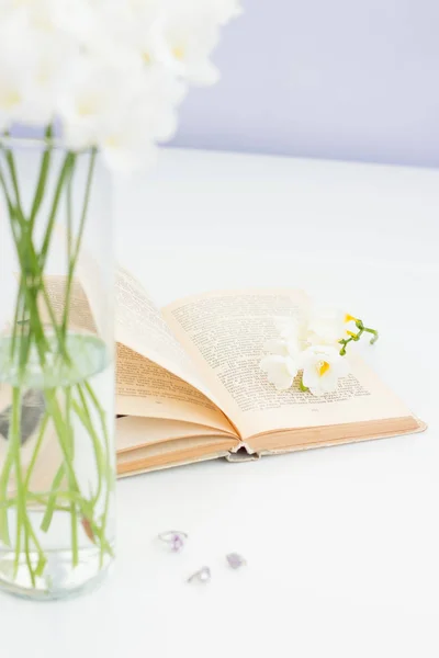 Ramo de flores blancas en un jarrón colocado sobre una mesa. Una foto acogedora. Ramo de flores blancas en un jarrón y un libro sobre una mesa blanca . — Foto de Stock
