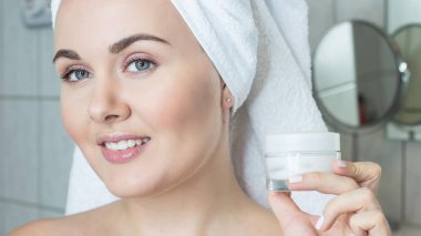 Kafasında bir havlu ile genç bir kadın. Kız krem yüzü. Bir kavanoz krem tutan bir kız.