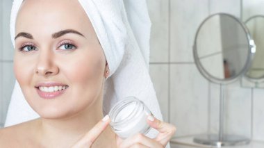 Kafasında bir havlu ile genç bir kadın. Kız krem yüzü. Bir kavanoz krem tutan bir kız.