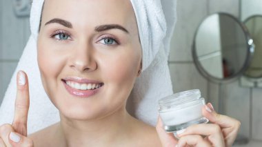 Kafasında bir havlu ile genç bir kadın. Kız krem yüzü. Bir kavanoz krem tutan bir kız.