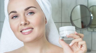 Kafasında bir havlu ile genç bir kadın. Kız krem yüzü. Bir kavanoz krem tutan bir kız.