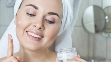 Kafasında bir havlu ile genç bir kadın. Kız krem yüzü. Bir kavanoz krem tutan bir kız.