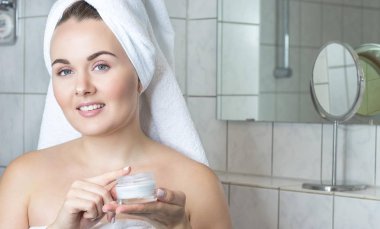 Kafasında bir havlu ile genç bir kadın. Kız krem yüzü. Bir kavanoz krem tutan bir kız.