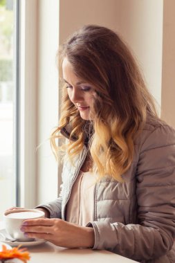 Bir kafede oturup güzel bir genç kadın. Kız içecekler Cappuccino.