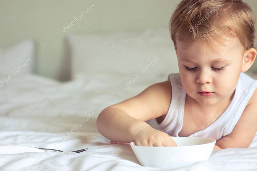 Little cute boy having breakfast in bed. Boy playing in bed. Breakfast in bed.