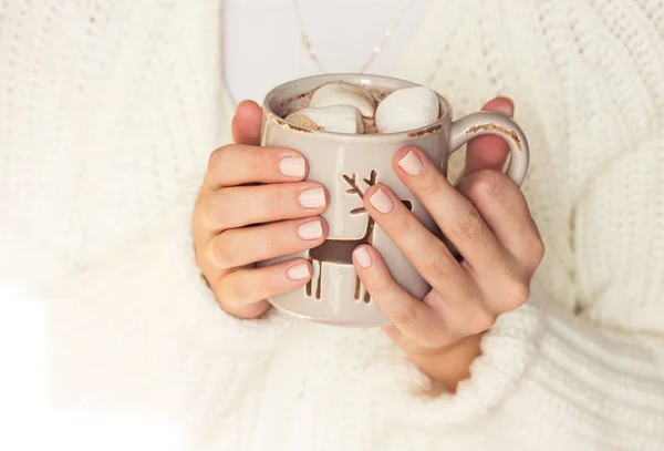 Junge schöne Frau in eine Strickdecke gehüllt und in der Hand einen Weihnachtsbecher mit heißem Kaffee und Marshmallows. Frauenhände — Stockfoto
