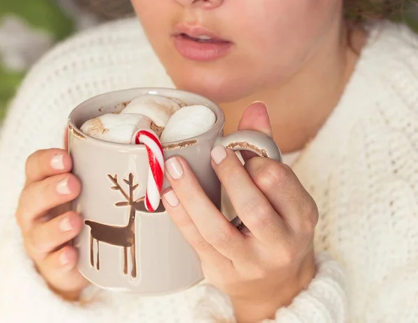 Junge schöne Frau in eine Strickdecke gehüllt und in der Hand einen Weihnachtsbecher mit heißem Kaffee und Marshmallows. Frauenhände — Stockfoto