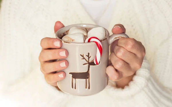 Junge schöne Frau in eine Strickdecke gehüllt und in der Hand einen Weihnachtsbecher mit heißem Kaffee und Marshmallows. Frauenhände — Stockfoto