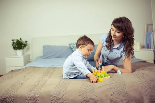 Ung mamma och unge son sitter på sängen. Mamma leker med sin son. Familj. — Stockfoto