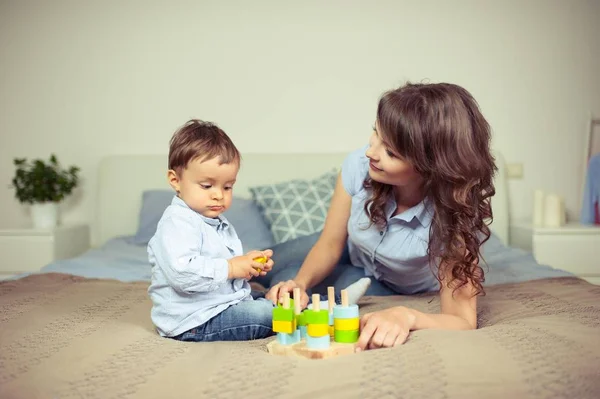 Ung mamma och unge son sitter på sängen. Mamma leker med sin son. Familj. — Stockfoto