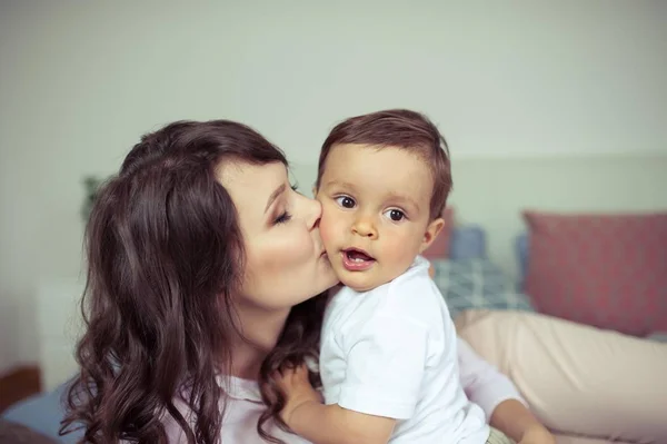 Genç anne ve genç oğlu yatağın üstüne oturmuş. Anne oğlu ile oynuyor. Aile.