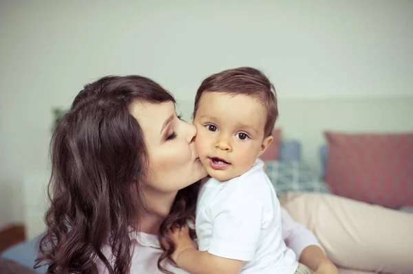 Genç anne ve genç oğlu yatağın üstüne oturmuş. Anne oğlu ile oynuyor. Aile.